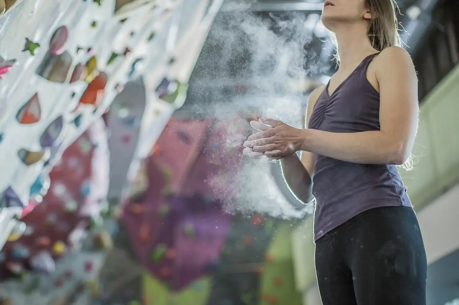 A person is in an indoor climbing gym, contemplating a climb. They have chalk on their hands