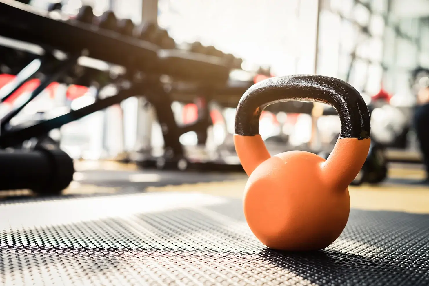 A kettleball sits on a floor in a gym environment